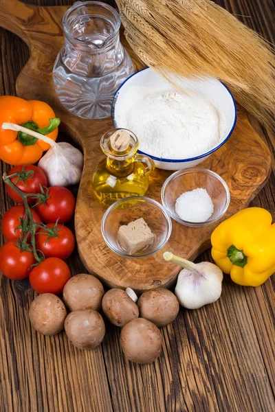 Fresh ingredients for a pizza dough and the pizza topping a wooden board made of olive wood with copy space in the lower part of the picture — Stock Photo, Image