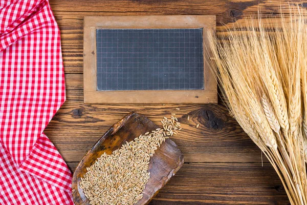 古いスレート黒板、穀物穀物と穀物の耳で非常に古い小麦粉スクープある赤白の市松模様のテーブル クロスで素朴な木材の背景コピー スペース — ストック写真