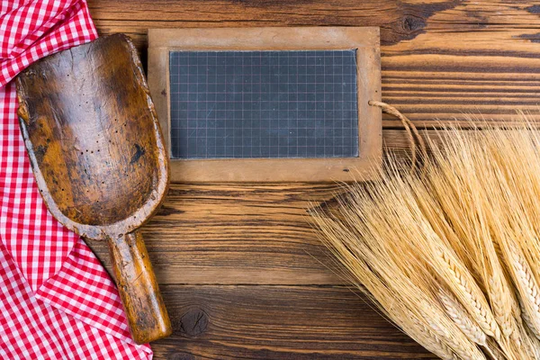 An old slate blackboard, a very old flour scoop and grain ears lie on a rustic wood background with a red white checkered tablecloth with copy space — Stock Photo, Image