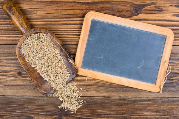 Een oud leien schoolbord en een zeer oude meelschep met graankorrels liggen op een rustieke houten achtergrond met kopieerruimte — Stockfoto