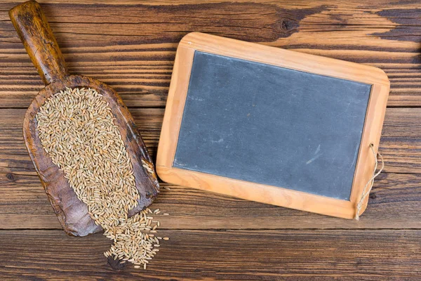 Een oud leien schoolbord en een zeer oude meelschep met graankorrels liggen op een rustieke houten achtergrond met kopieerruimte — Stockfoto