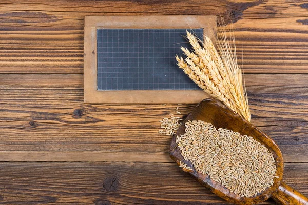 Un vieux tableau noir en ardoise, une très vieille cuillère à farine avec des grains de céréales et des épis de grain reposent sur un fond de bois rustique avec espace de copie — Photo