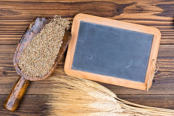 Eine alte Schiefertafel, eine sehr alte Mehlschaufel mit Getreidekörnern und Getreideähren liegen auf rustikalem Holzhintergrund mit Kopierraum — Stockfoto