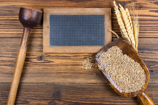 Eine alte Schiefertafel, eine sehr alte Mehlschaufel mit Getreidekörnern und Getreideähren liegen auf rustikalem Holzhintergrund mit Kopierraum — Stockfoto