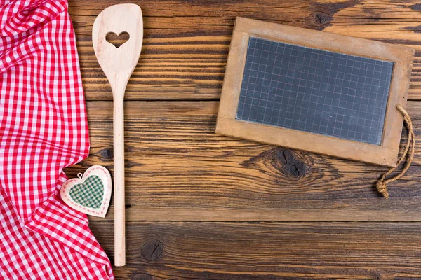 Vecchia lavagna rustica in ardesia con cucchiaio da cucina in legno su tessuto a quadretti bianco rosso su sfondo vecchio in legno con spazio copia — Foto Stock