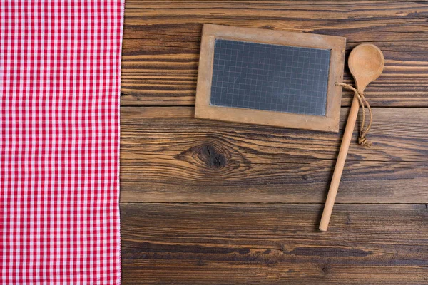 Oude leisteen bord en een houten koken lepel op rustieke houten achtergrond aan de linkerkant ligt een doek rood wit checered — Stockfoto