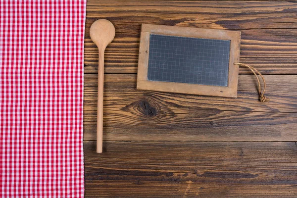 Eski rustik ahşap arka plan ile bir ahşap yemek kaşık ve bir eski kayrak yazı tahtası. Sol tarafında kırmızı beyaz kareli kumaş vardır. Kopya alanı kayrak tahtaya ve resmin alt alanı ile — Stok fotoğraf