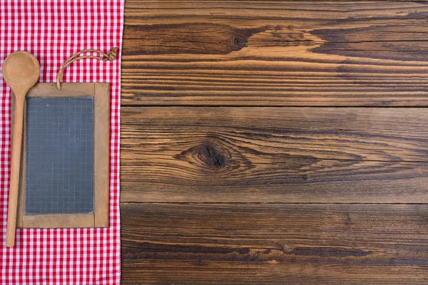 Velho quadro-negro de ardósia e uma colher de cozinha de madeira no fundo de madeira rústica no lado esquerdo encontra-se um pano vermelho branco xadrez — Fotografia de Stock