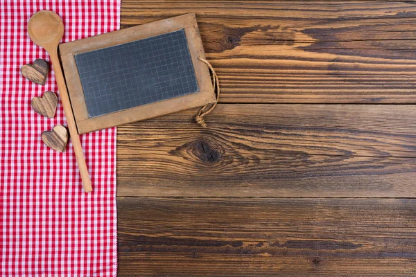 Alte rustikale Schiefertafel mit Kochlöffel auf rot-weiß kariertem Stoff auf altem Holzhintergrund mit Kopierraum im rechten Bildbereich — Stockfoto