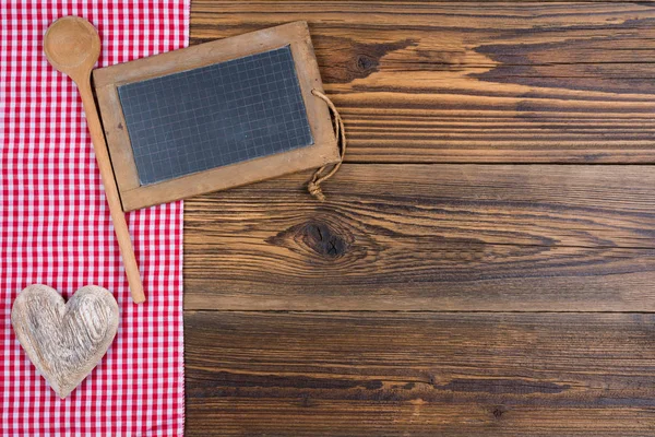 Velho quadro-negro de ardósia rústico com colher de cozinha de madeira em tecido xadrez branco vermelho no fundo de madeira velha com espaço de cópia na área direita da imagem — Fotografia de Stock