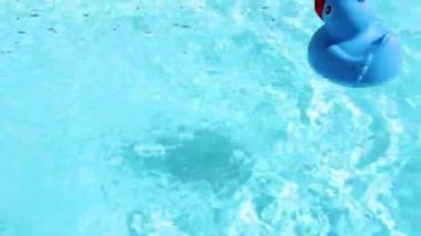 A blue rubber duck floats into the picture from the right and can be drifted easily on the crystal clear water of a pool