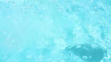 A single Black Rubber Duck is swimming from the right to the left on crystal clear pool water