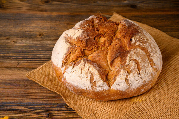 A fresh whole grain bread from the baker on a jute fabric on a rustic wooden background
