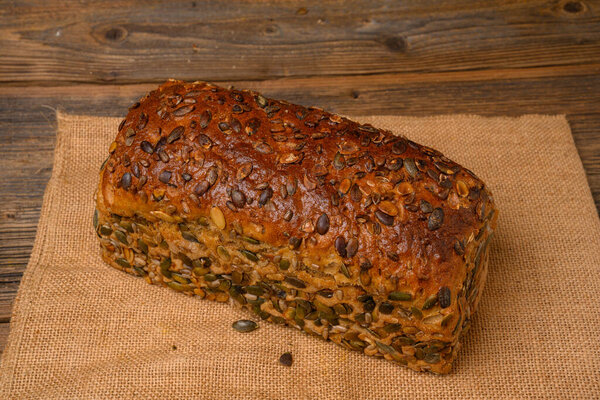 A fresh pumpkin seed bread from the baker on a jute fabric on a rustic wooden background.