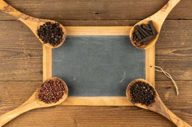 Farklı biberli zeytin ağacından yapılmış dört ahşap kaşık ve kırsal ahşap arka planda fotokopi alanı olan eski bir siyah tahta.