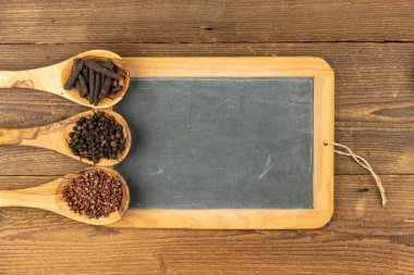 Farklı biberli zeytin ağacından yapılmış üç ahşap yemek kaşığı ve kırsal ahşap arka planda fotokopi alanı olan eski bir siyah tahta tahta.