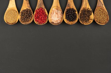 Çeşitli baharatlarla doldurulmuş zeytin ağacından yapılmış yedi yemek kaşığı fotokopi alanı olan siyah bir arka planda duruyor.