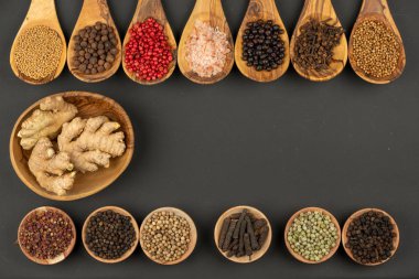 Arka arkaya yedi yemek kaşığı zeytin ağacından ve çeşitli baharatlarla dolu altı küçük ahşap kase ve siyah arka planda zencefil kökü ve fotokopi alanı olan ahşap bir kase.