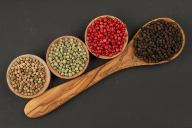 Siyah biberli zeytin ağacından yapılmış bir yemek kaşığı ve fotokopi alanı olan siyah arka planda yeşil, kırmızı ve beyaz biberlerle dolu üç ahşap kase.