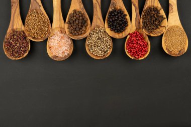 Baharat ve Gıda - Siyah arka planda, arkaplanda baharat ve biber çeşitleriyle dolu, zeytin ağacından yapılmış dokuz kaşık.