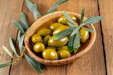 Zeytinyağındaki yeşil zeytinleri ve kırsal ahşap arka plandaki küçük bir zeytin kabındaki zeytin dalını kapat.