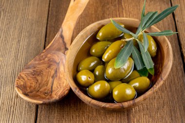 Zeytinyağlı yeşil zeytinyağı küçük bir ahşap kasede zeytin dalı ve kırsal ahşap arka planda zeytin ağacından yapılmış bir yemek kaşığı.