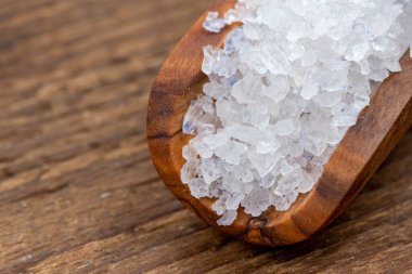 Kırsal ahşap arka planda zeytin ağacından yapılmış küçük bir baharat küreğinin üzerindeki kaba kristal tuz yakın plan.