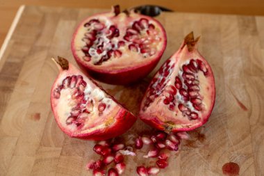 Ön planda nar tohumu ve ahşap bir kesim tahtasının üzerinde çeyrek nar meyvesi olan bir ev mutfağını kapatın.