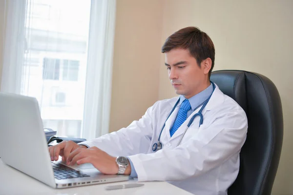 Docteur souriant posant dans le bureau, il porte un stéthoscope — Photo