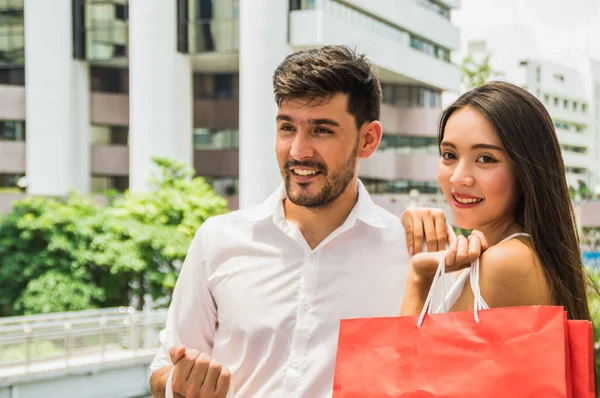 Happy young couple with shopping bags walking in mall — Stock Photo, Image