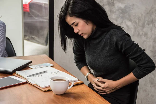 Молодая азиатская деловая женщина с болью в животе в офисе — стоковое фото