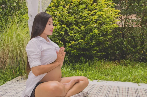 Pregnant women are playing yoga in the garden.