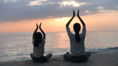 Anne ve kızının silueti akşam deniz kenarında yoga yapıyor. 4k Çözünürlüğü.