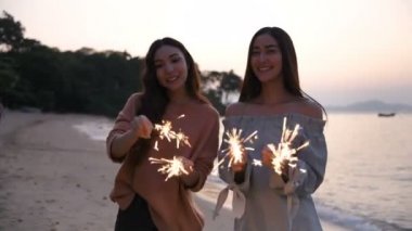 Tatil konsepti. Kız sahilde havai fişeklerle mutlu bir şekilde oynuyor. 4k Çözünürlüğü.