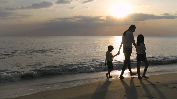 La silhouette di una madre e un bambino che camminano sulla spiaggia nel — Foto Stock