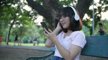 Tatil konsepti. Asyalı kız halk bahçelerinde müzik dinlemekten zevk alıyor. 4k Çözünürlüğü.