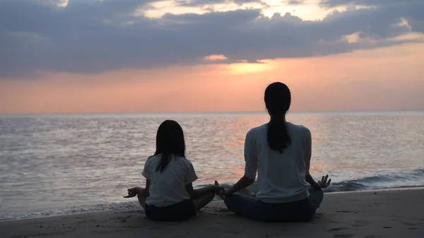 Silhueta de mãe e filha fazendo ioga junto ao mar no e — Fotografia de Stock
