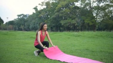 Egzersiz kavramları. Parkta yoga minderleri döşeyerek egzersiz yapmaya hazırlanan genç kadınlar. 4k Çözünürlüğü.