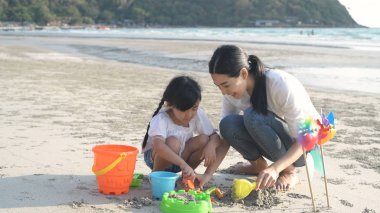 Tatil konsepti. Anne babaları ve kızları kumsalda kum oynuyorlar.