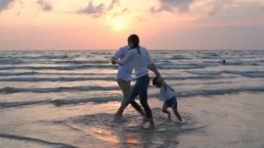Tatil konsepti. Anne ve baba sahilde koşup kızlarıyla oynuyorlar. 4k Çözünürlüğü.