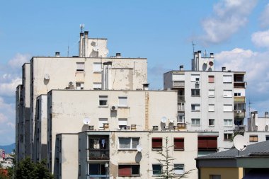 Şehrin eski kesiminde, bulutlu mavi gökyüzü arka planında güneşli yaz gününün çeşitli boyutlarda uydu antenleri ve bacaları olan harap haldeki beyaz apartmanlar.