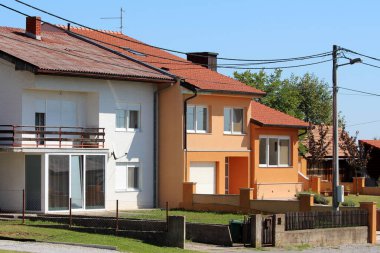 Yeni ve yenilenmiş renkli beyaz ve turuncu renkli banliyö aile evleri, geniş cam yüzeyler ve açık mavi gökyüzü arka planında çimenler.