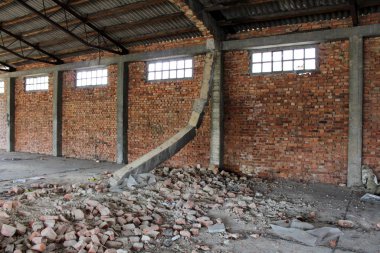 Sıcak yaz gününde eski terk edilmiş sanayi hangarında yıkılmış destek kirişi ve içindeki kırmızı tuğla duvar inşaat malzemeleriyle çevrili.