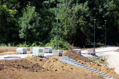 İnşaat halindeki yeni halka açık kaldırımda, orta büyüklükteki konteynır veya metal kafesli İbc plastik tankı ve yeşil sokak lambaları ve kuru toprak ile çevrili beton basamakların yanına yerleştirilmeye hazır taş fayanslar bulunuyor.