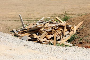 İnşaat sahasında bırakılan kırık tahta yığını sıcak yaz gününde çakıl ve kuru toprakla çevrili.