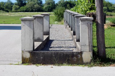 Tamamlanmamış sıralar halinde beton çit direkleriyle çevrili. Evin arka bahçesinde çimenler ve çakıllarla çevrili.