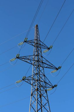 Açık mavi gökyüzü arka planında, uzun şeffaf cam yalıtkanlara bağlı yedi elektrik kablosu ile metal borulardan yapılmış büyük bir elektrik hattı elektrik direği.
