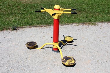 Üçlü Twister renkli kırmızı ve sarı halka açık park spor ekipmanları. Çevrelerinde çakıllar ve yerel parktaki yeni kesilmiş çimenler var.