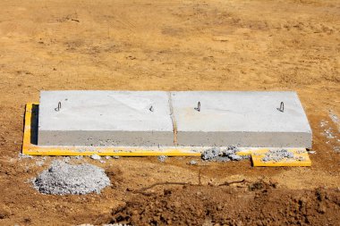 İki büyük, uzun, beton rögar kapağı. Yerel inşaat alanındaki kuru toprakla çevrili tahta tahtaların üzerinde metal kancalar var.