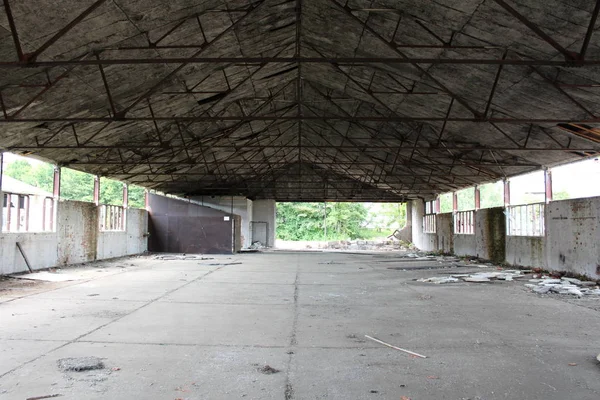 Inside of large empty military hangar with destroyed inner walls and missing windows at abandoned military complex on warm sunny summer day